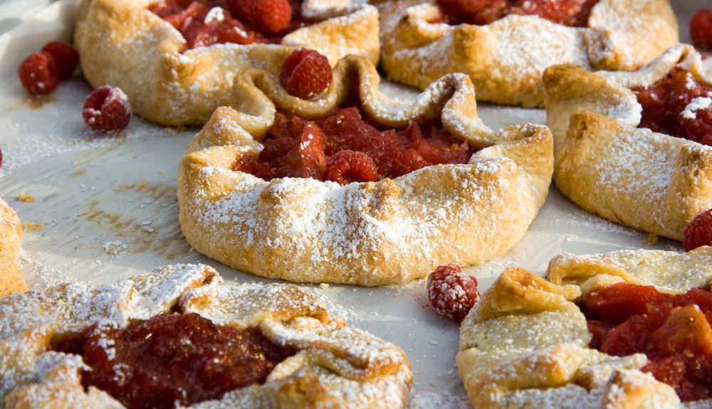 Fresh raspberry tarts with a sprinkling of powdered sugar sit cooling on a parchment-lined baking tray