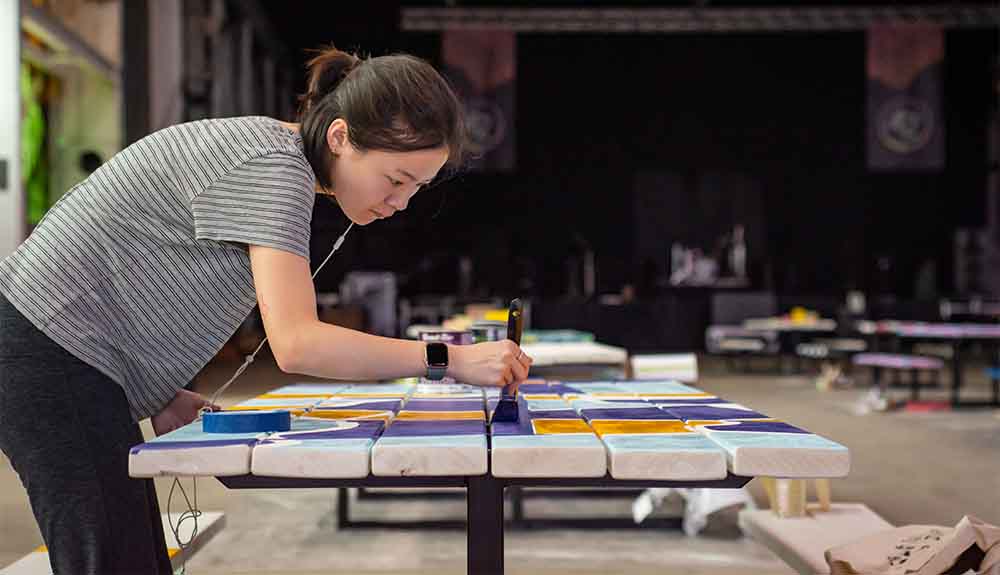 A woman is shown painting a picnic table