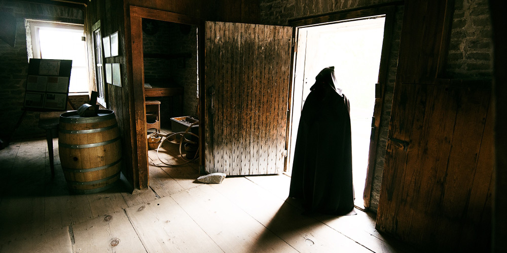 Creepy person in a cloak walks out of a wooden room