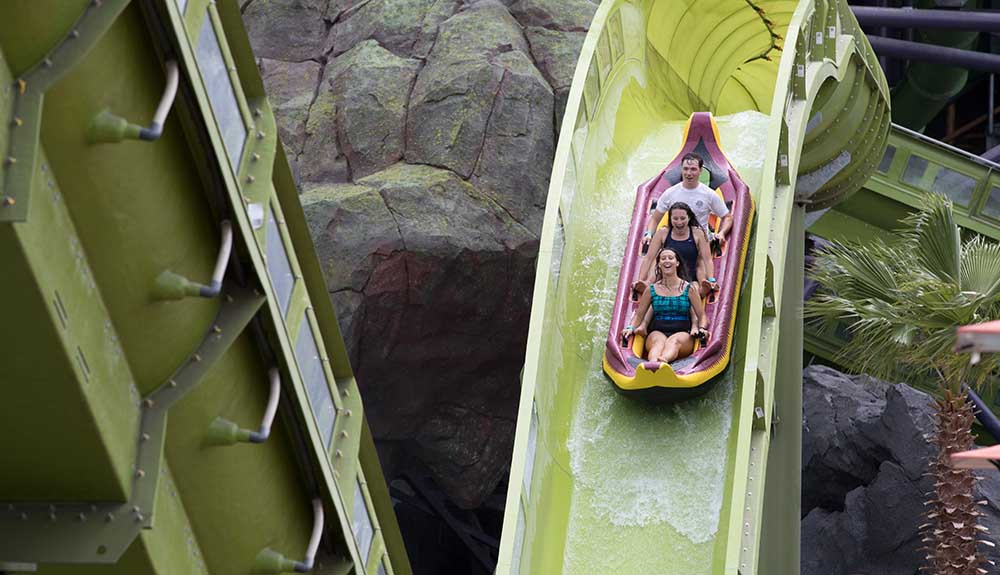 Man, woman and child ride a plastic floating device down a water slide