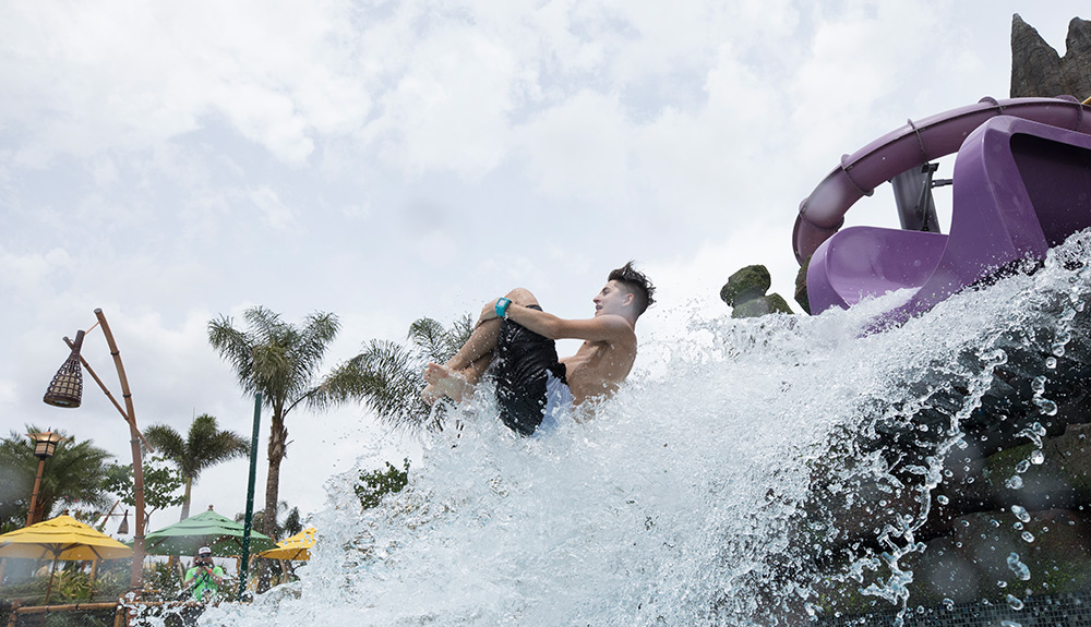 A man in swim trunks comes shooting out of a purple slide at Universal Orlando Resort