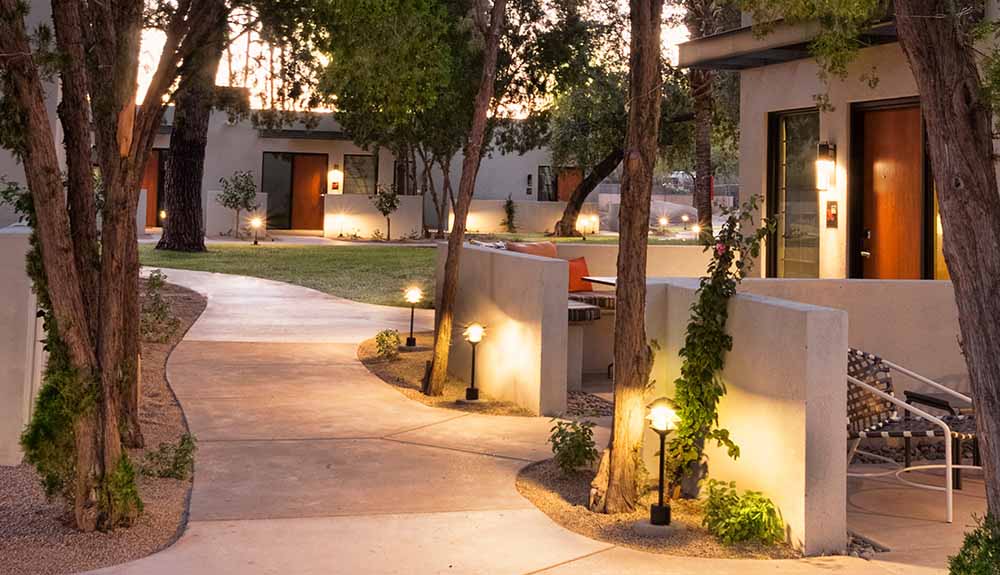 A quiet walkway leading to individual cottages is lit up with garden lights at dusk