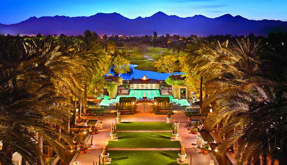 The Scottsdale Resort is seen at night, palm trees lining the beautiful ground and the pool glowing in the early evening light