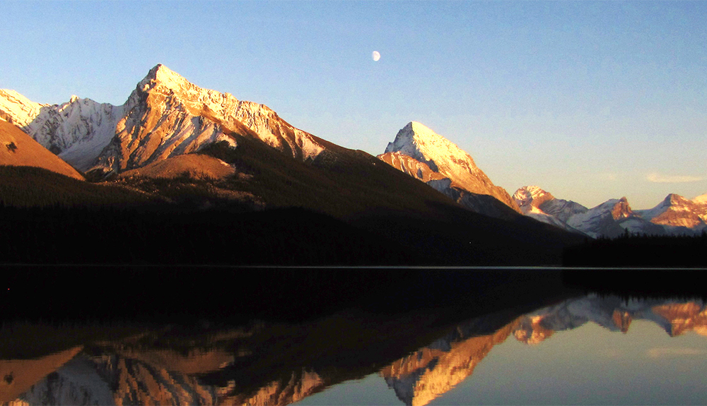 Photo submitted by Caleb Crawley of a moonrise over Maligne Lake, the mountains looking majestic over the still waters