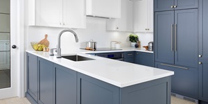 A clean and contemporary kitchen with white countertop, blue-grey painted wooden cabinets and simple silver fixtures