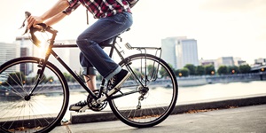 Closeup shot of a person in plaid shirt and cuffed jeans riding a black city bike along the Portland waterfront at sunset, the cityscape seen in the background