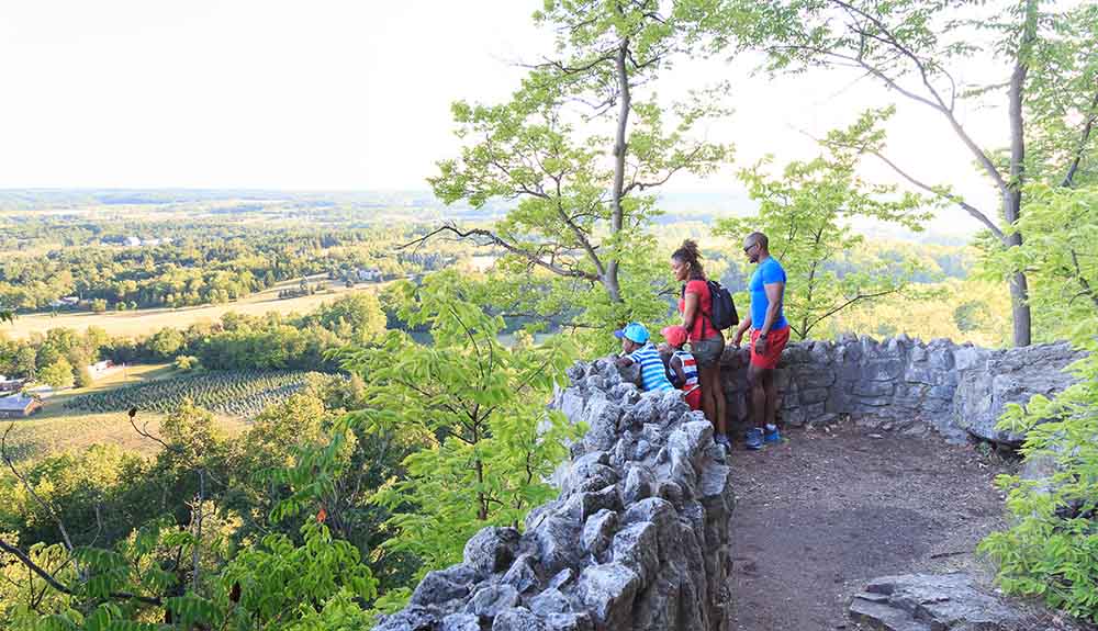 Viewpoint with a balcony made of rocks with two adults and a small child looking out at Rattlesnake Point Conversation Area
