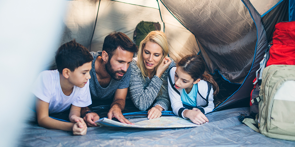 Two kids and two adults lying on their stomachs looking at a map in a tent facing the opening