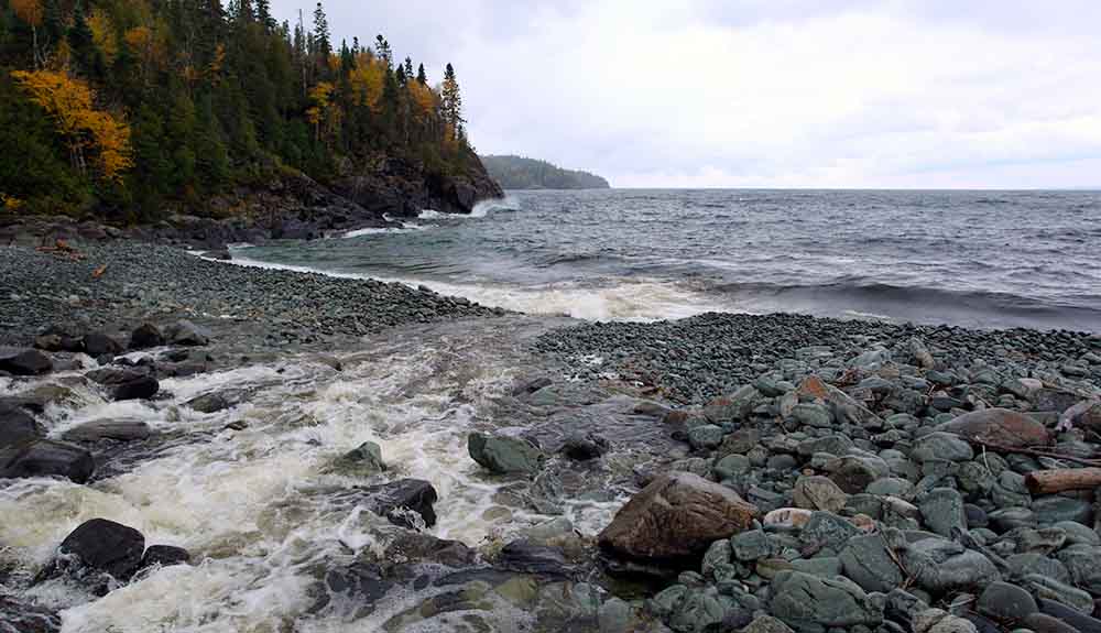 Many rocks on greenstone beach with a stream that runs into Lake Superior