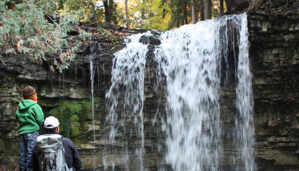 Two people watch the Hilton Falls close up in the conservation area