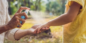 Parent spraying child's arm with insect repellent