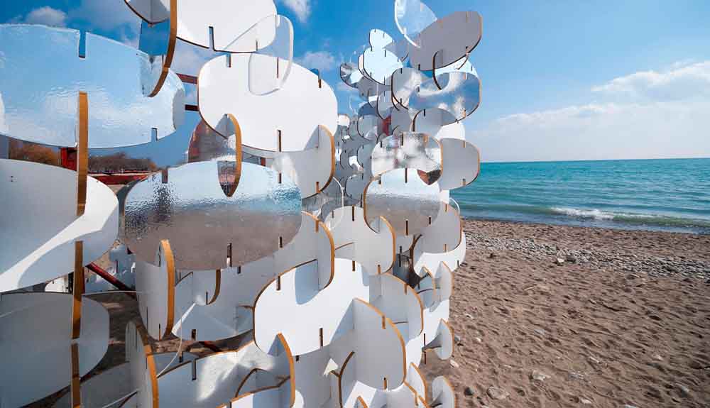 A mirrored sculpture is shown on a beach