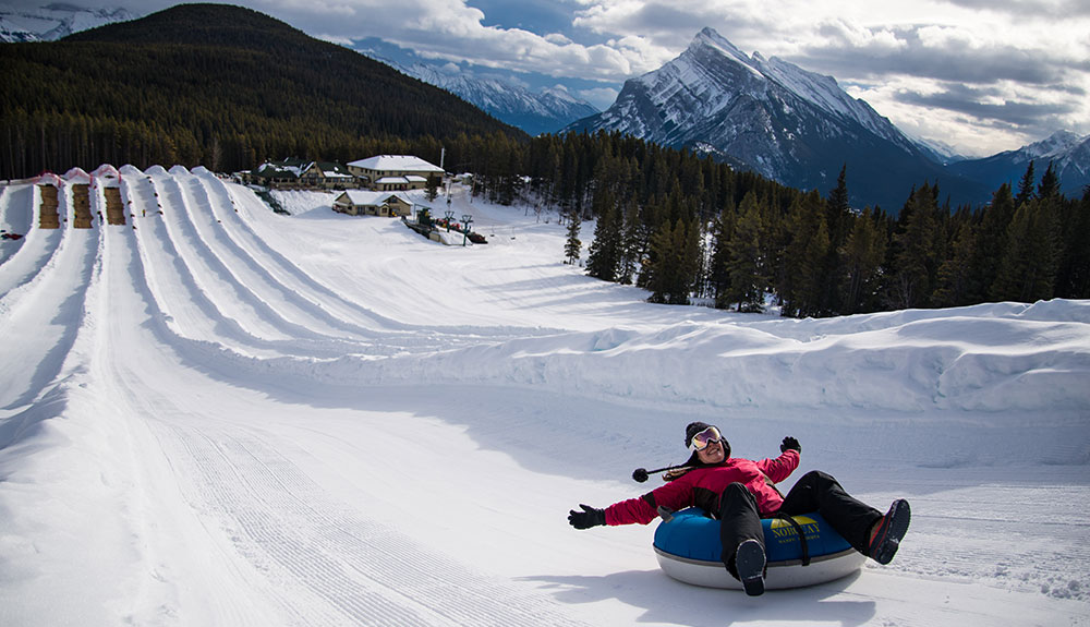 Person in red winter coat and snow pants slides down a snowy hill on a tube