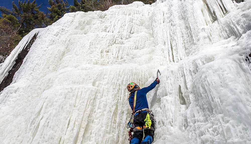 Person holding a sharp tool as they scale a frozen wall ice climbing