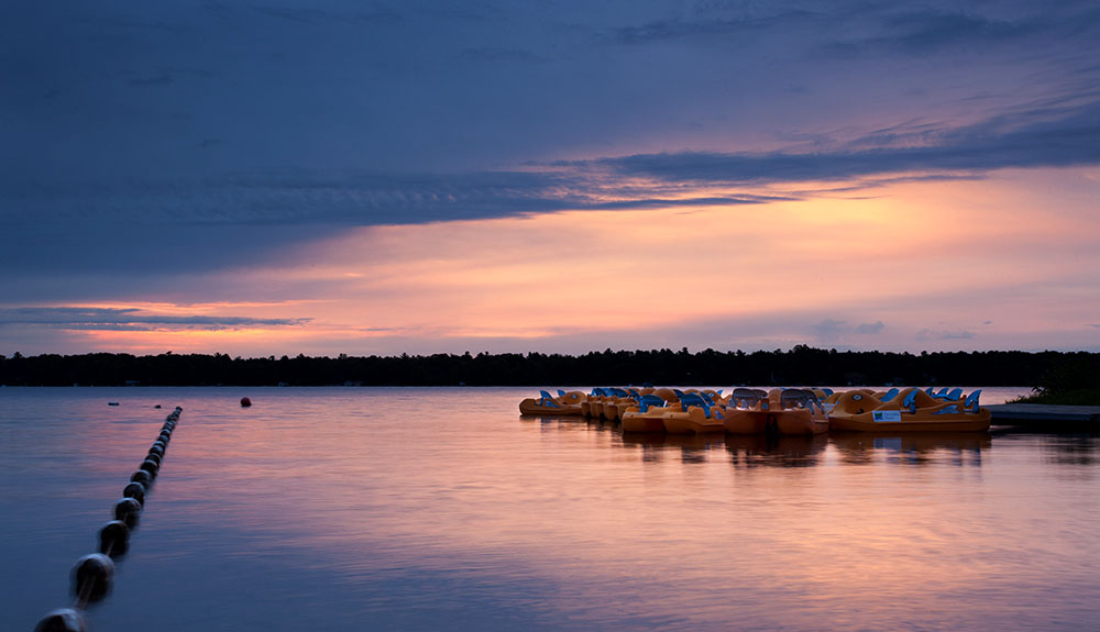 Paddleboats rest on calm water at sunset