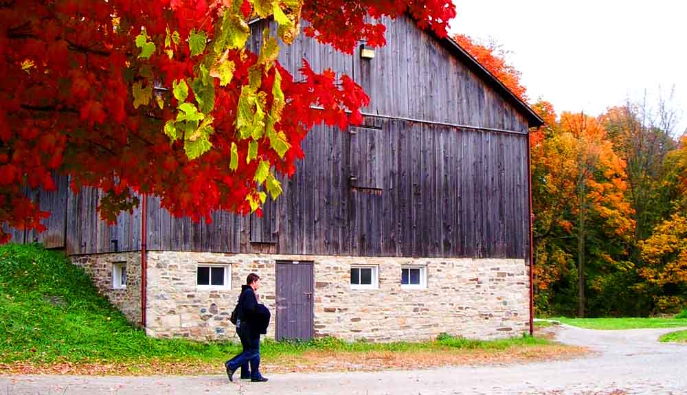 Two people walking by a big barn on a hill in the fall