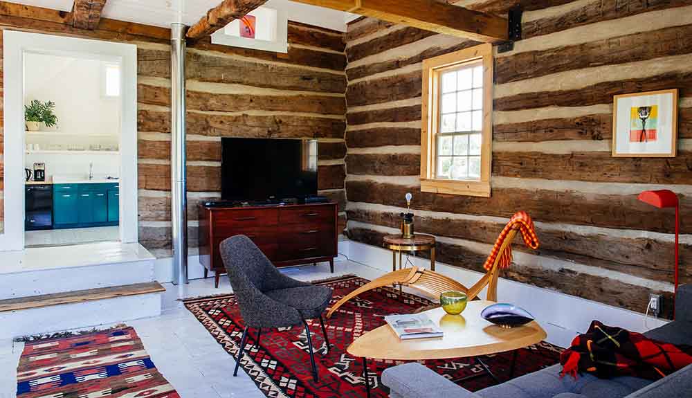 Rustic wooden cabin with television, chair and sofa, a light kitchen seen in the background