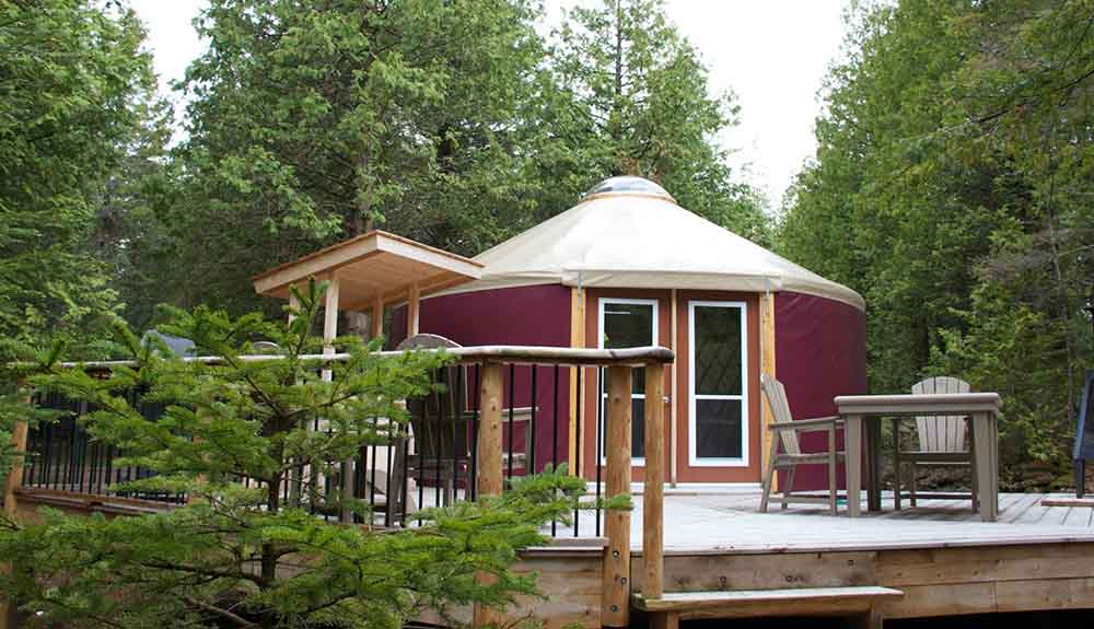 Dark red yurt beside a wooden deck in the forest at Bruce Peninsula National Park