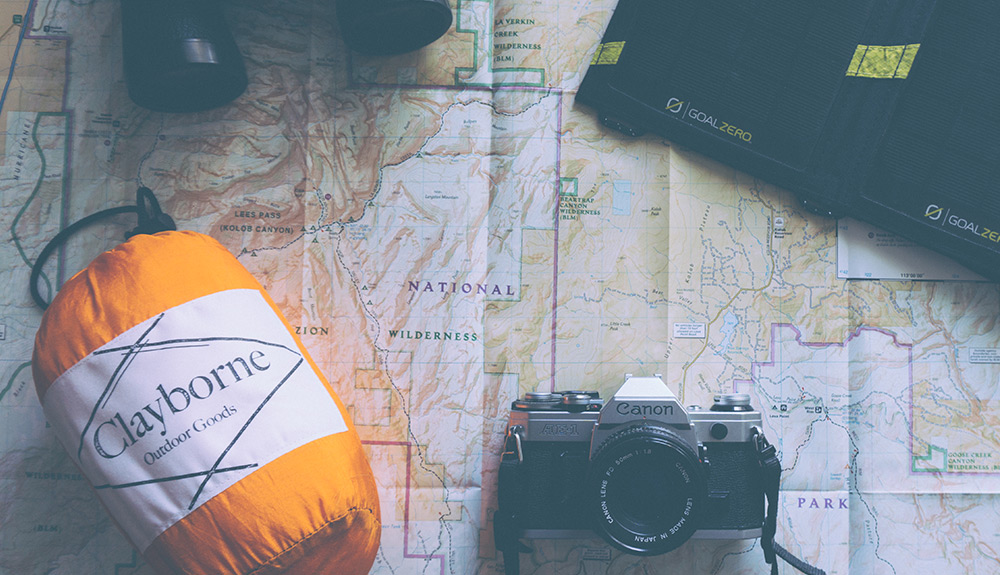 Orange Clayborne sleeping bag, camera, binoculars and a laptop seen on top of a paper map