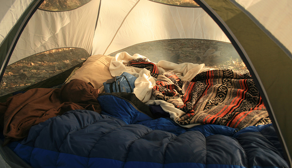 The interior of a tent, the floor lined with sleeping bags and cozy blankets