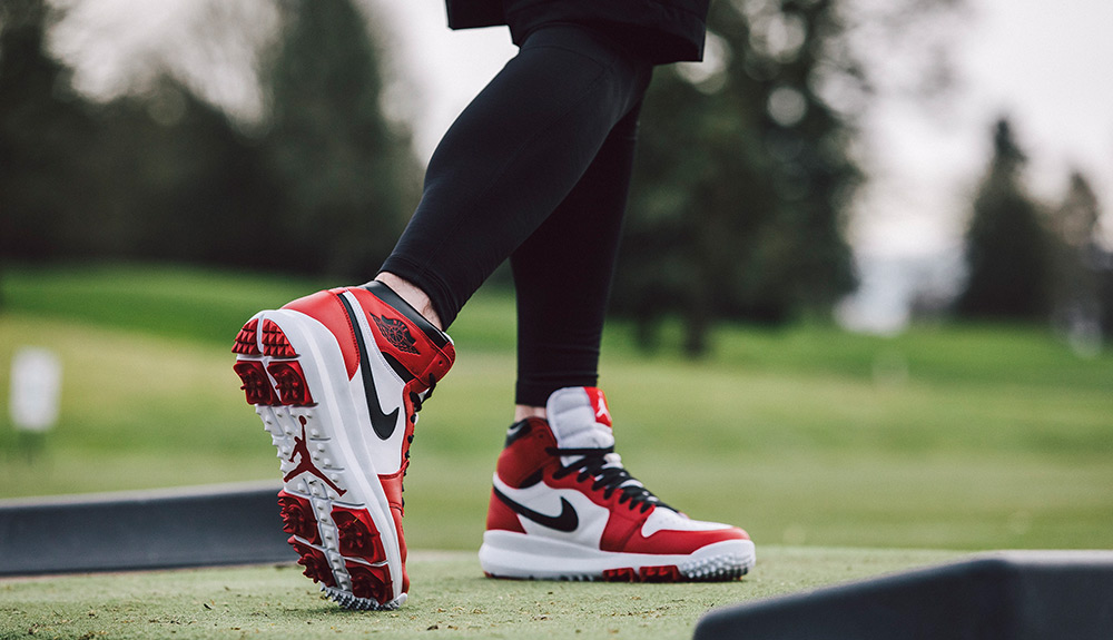 Red, white and black Nike Air Jordan 1s are seen worn by a person on a golf course