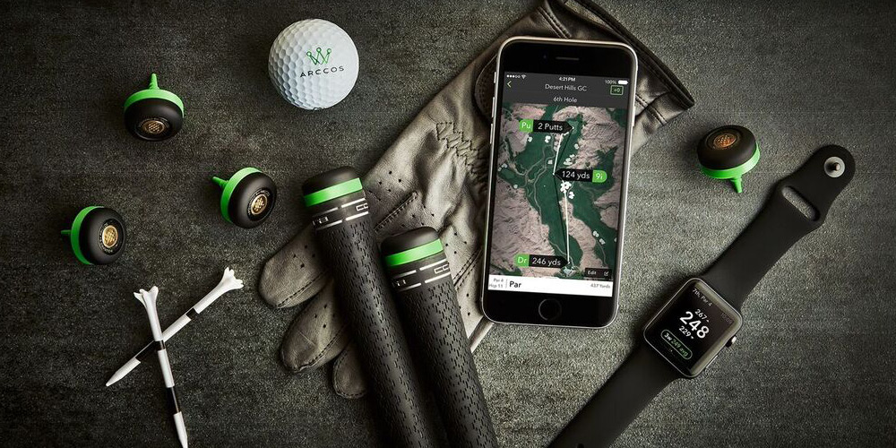 Various golfing tools including golf balls, smart phone and smartwatch are laid out on a table