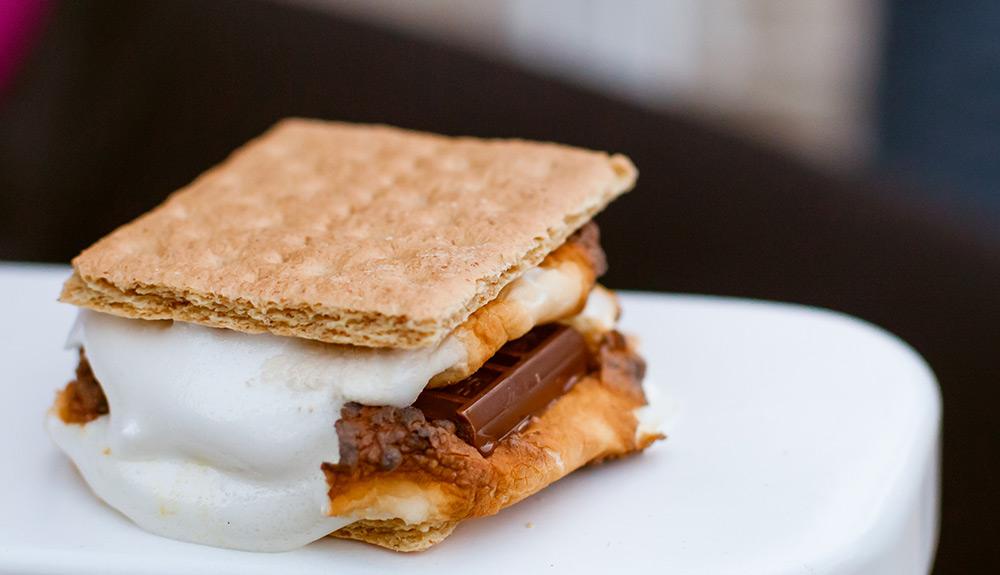 A smore is seen with a toasted graham cracker, oozing marshmallows and milk chocolate piece
