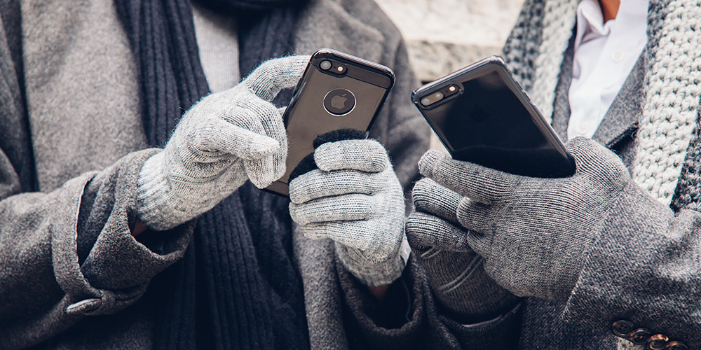 The hands of two people are seen, both clad in grey gloves, jackets and scarves as they tap away on their smartphones