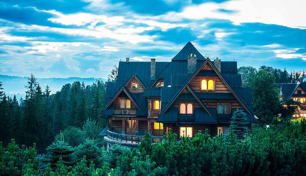 Big cottage with the lights on surrounded by trees as the day fades into night