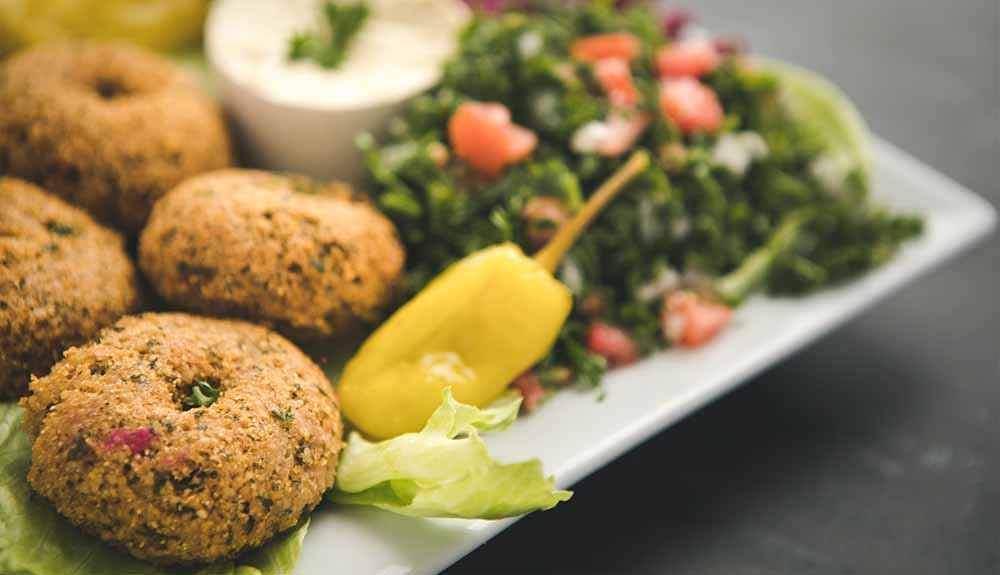 A plate with crispy falafels with a side of a green chopped salad with a small pepper next to it and a bowl of white dip.