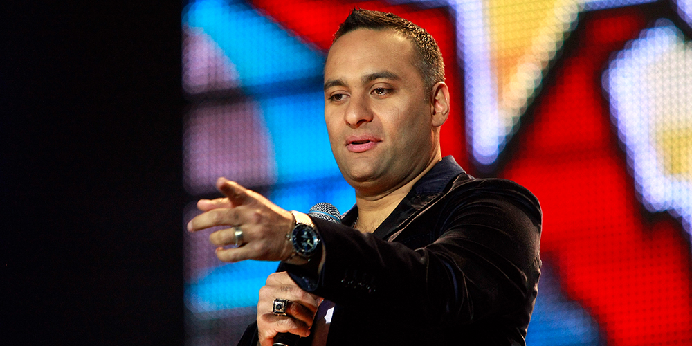 Russell Peters pointing while holding a mic on stage