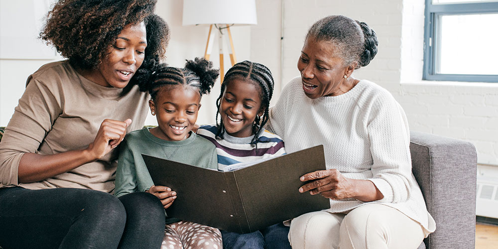 Multi-generational family featuring a grandma, mom and two little girls looking at a big book
