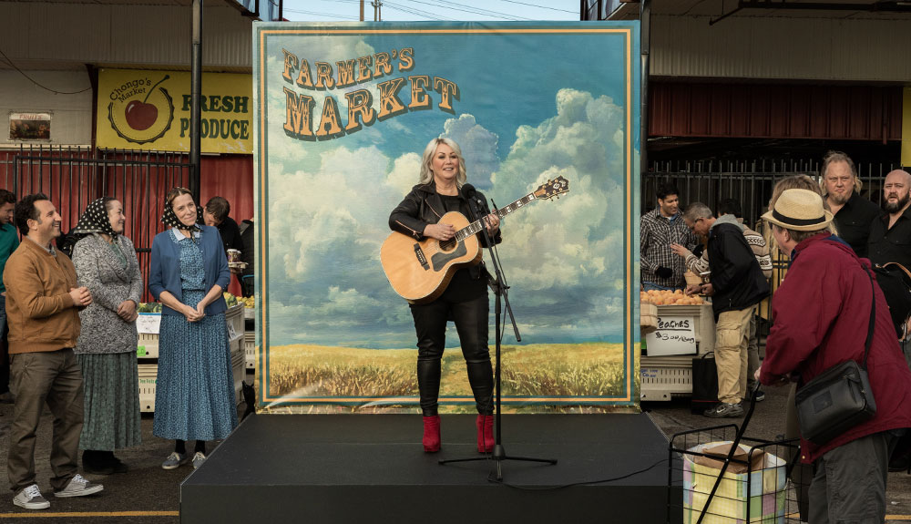 Jann Arden performs on a small stage at a farmer's market