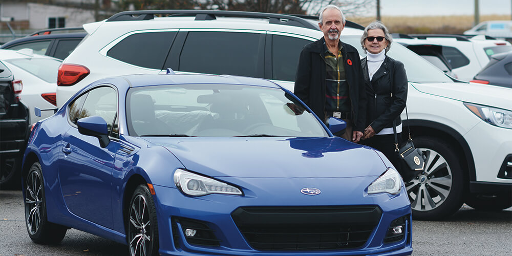 CAA Give and Get contest winners Randy and Linda Ward standing with a blue Subaru BRZ sports car at Whitby Subaru in Ontario