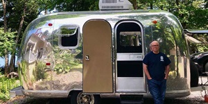 Terry O'Reilly host of CBC Radio One stands outside of his metal vintage trailer