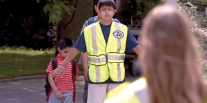 A teenaged boy wearing a lime green, CAA-branded safety vest, directing children behind him.