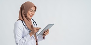A doctor wearing a white lab coat and a black stethoscope around her neck holds a patient file and reads it.