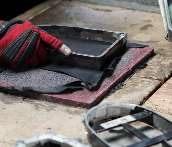 A hand wearing a red glove using a template to cut a piece of black leather.