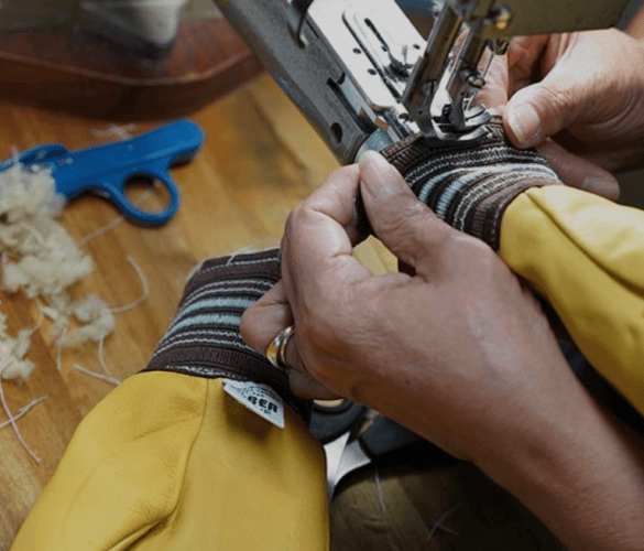 A person's hands holding a pair of yellow mittens, feeding them into a sewing machine.
