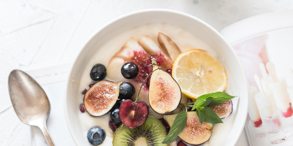 A breakfast bowl with fresh figs, blueberries, kiwi, orange, sliced apples and sprig of mint