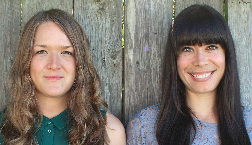 Authors Lindsay Anderson and Dana VanVeller pose in front of a wooden fence