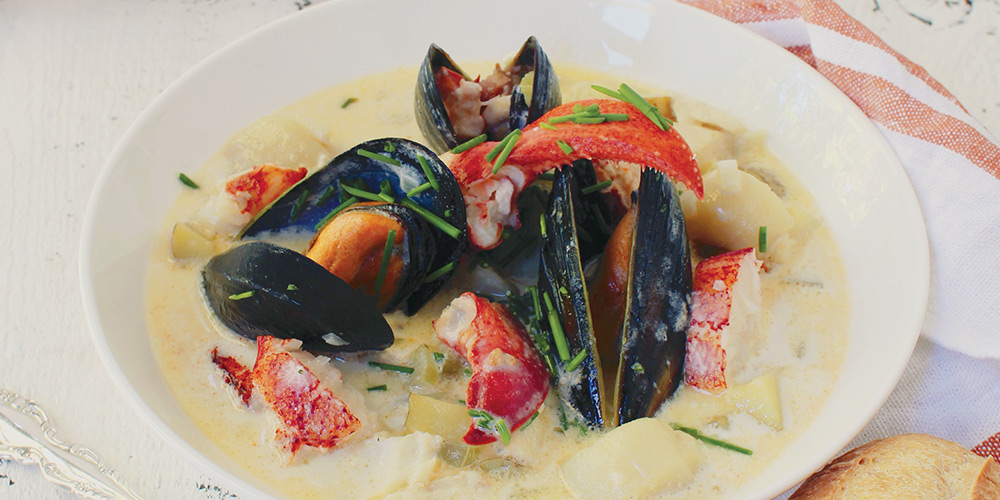 A bowl of seafood chowder, large chunks of lobsers and large clams, shell open 