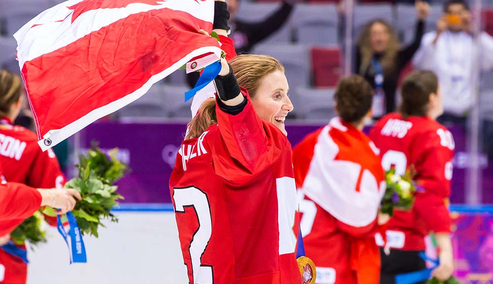 Hayley Wickenheiser waves the Canadian flag behind her as she skates around in victory