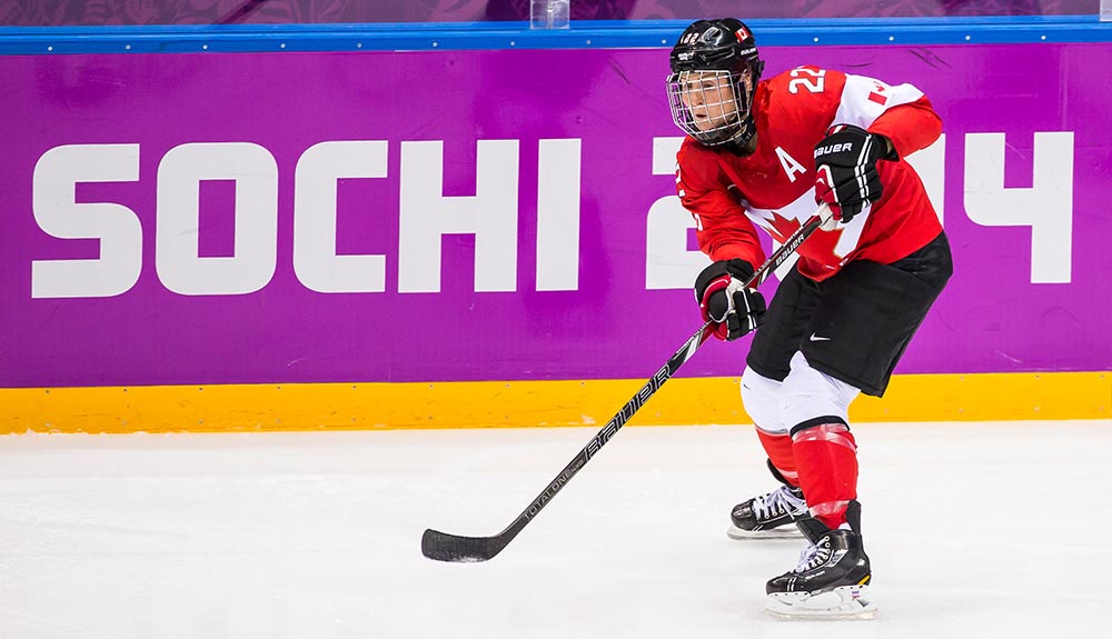 Hayley Wickenheiser on the ice wearing hockey gear, her hockey stick at the ready in front of her