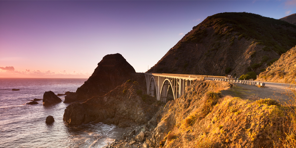 A big bridge continues the road on the California coast at sunset