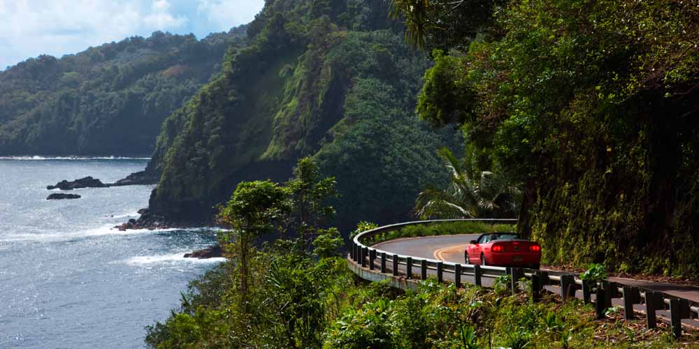 Red convertible drives on the Hana Highway along the coast of Maui.