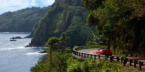 Red convertible drives on the Hana Highway along the coast of Maui