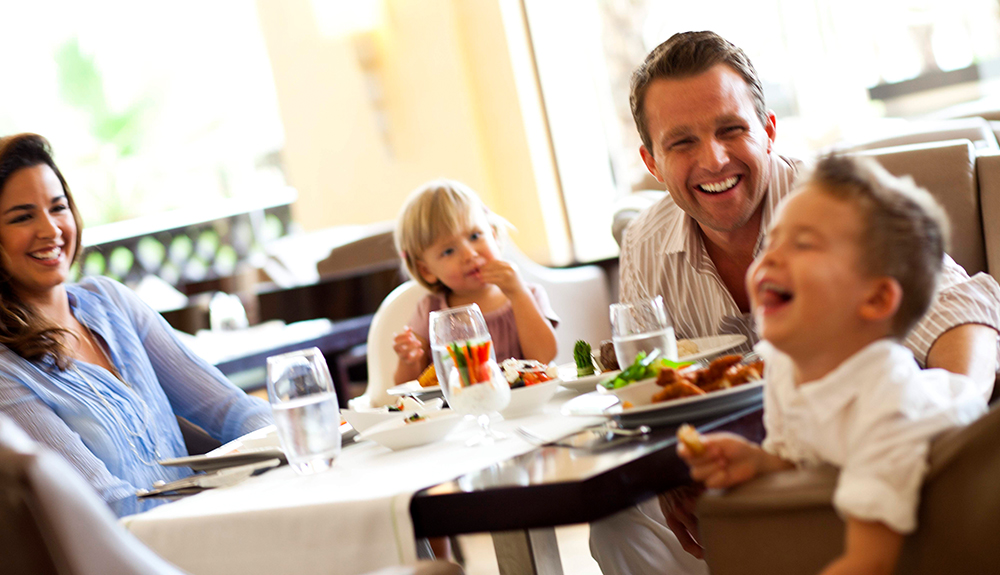 Family of four laughing over dinner at a restaurant