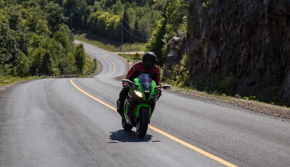 A sporty green motorcycle speeds down an empty winding road in the Kawartha Lakes region