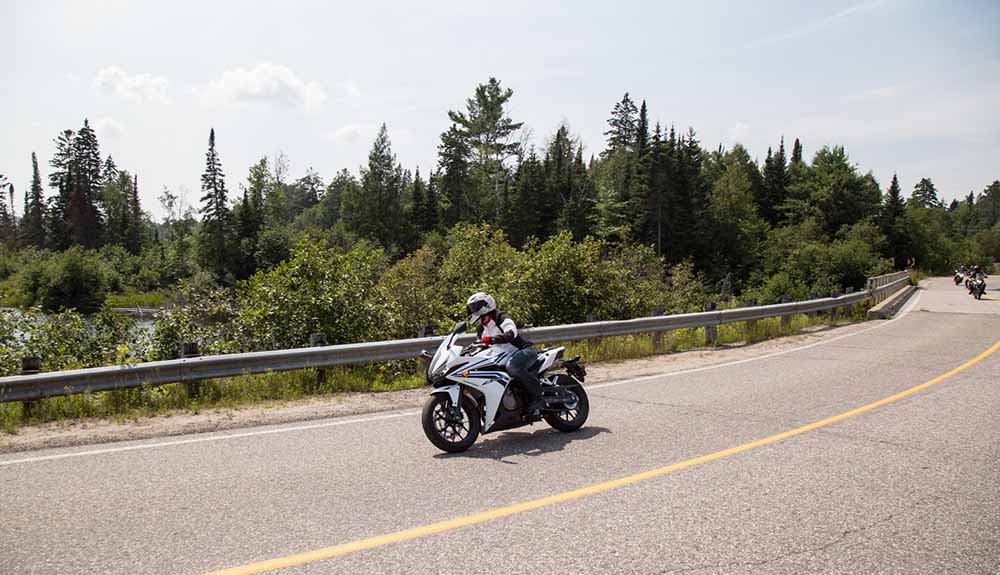 A sporty silver motorcycle takes a wide right turn on the tree-lined Riding and Relaxation trail
